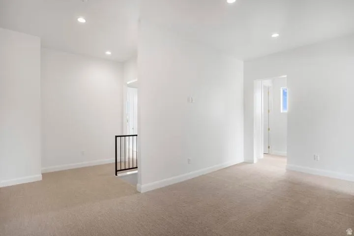 Open concept space featuring neutral carpeting, recessed lighting, white walls, white baseboards, and a black metal railing