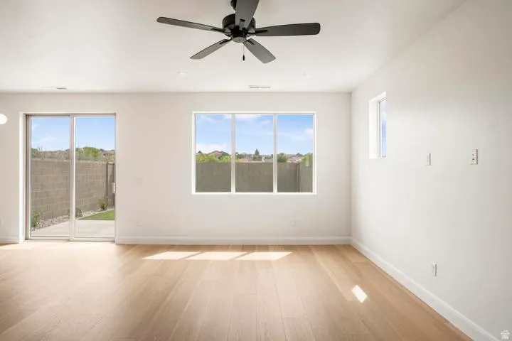 Spacious interior room featuring light wood-finish flooring, a contemporary black ceiling fan, and white walls