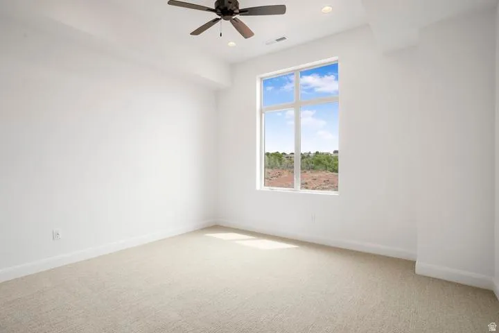 Bright interior space featuring a large multi-pane window, neutral carpet flooring, recessed lighting, and a ceiling fan with integrated lighting