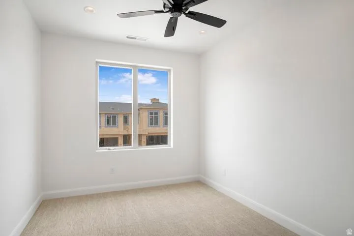 Bright room featuring a large window, neutral carpeting, white baseboards, a black ceiling fan, and recessed lighting
