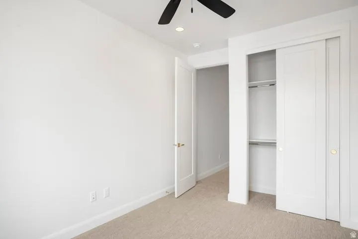 Carpeted interior space featuring white walls and trim, a dual-door closet with shelving, a white interior door with brass hardware, and a ceiling fan with recessed lighting