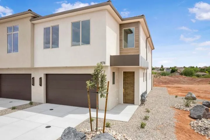 Modern stucco exterior featuring two garage bays, a contemporary wooden entry door, and a decorative balcony