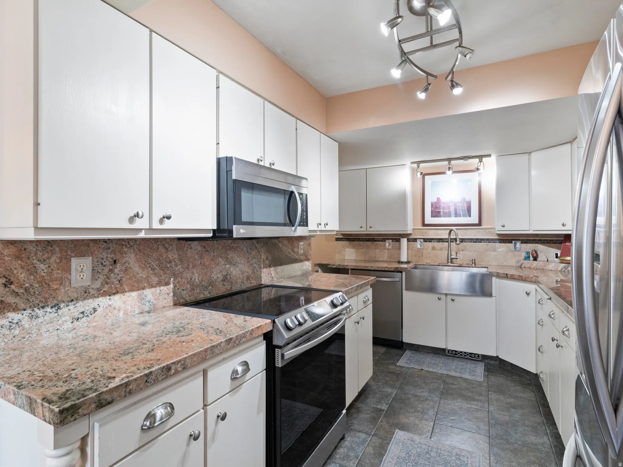 Kitchen featuring extensive white cabinetry, Granite countertops, stainless steel appliances, a stainless steel farmhouse sink, and tile flooring