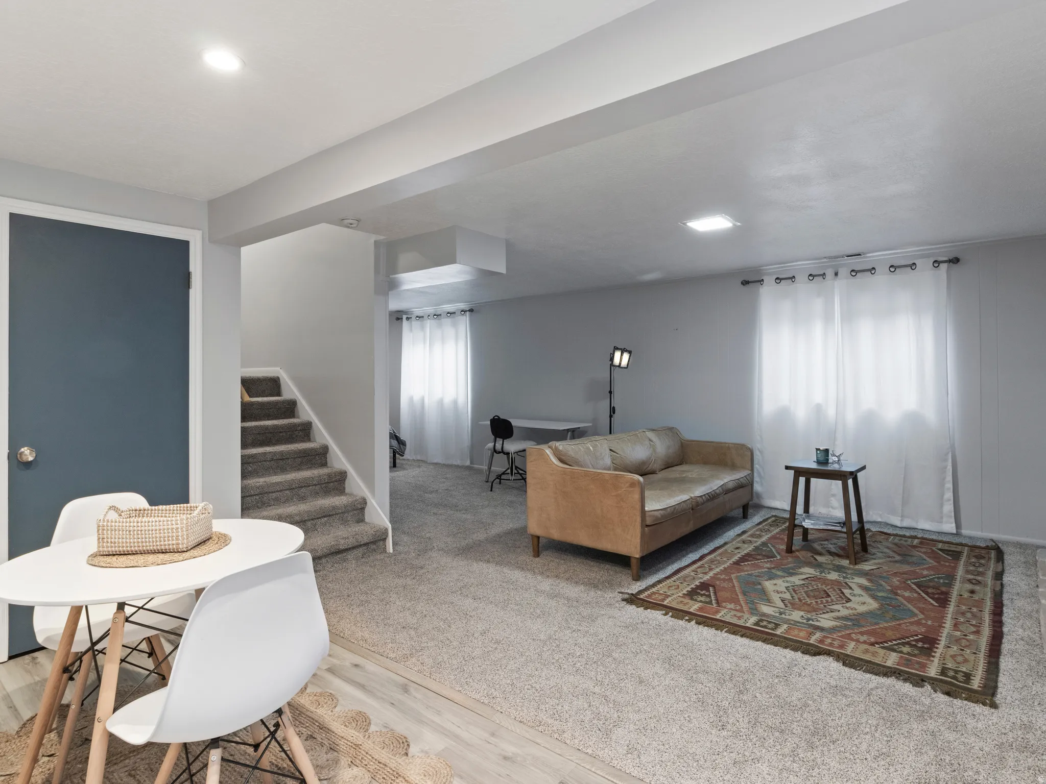 Spacious living area featuring light gray walls, recessed lighting, and a blend of light wood-finish flooring and neutral carpeting