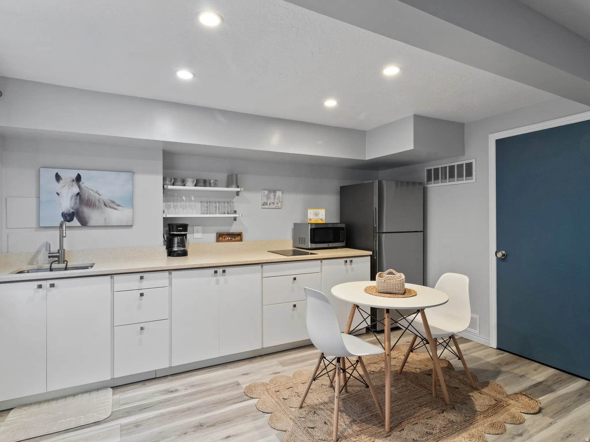 Contemporary kitchen area featuring extensive white cabinetry, light countertops, and laminate finish flooring
