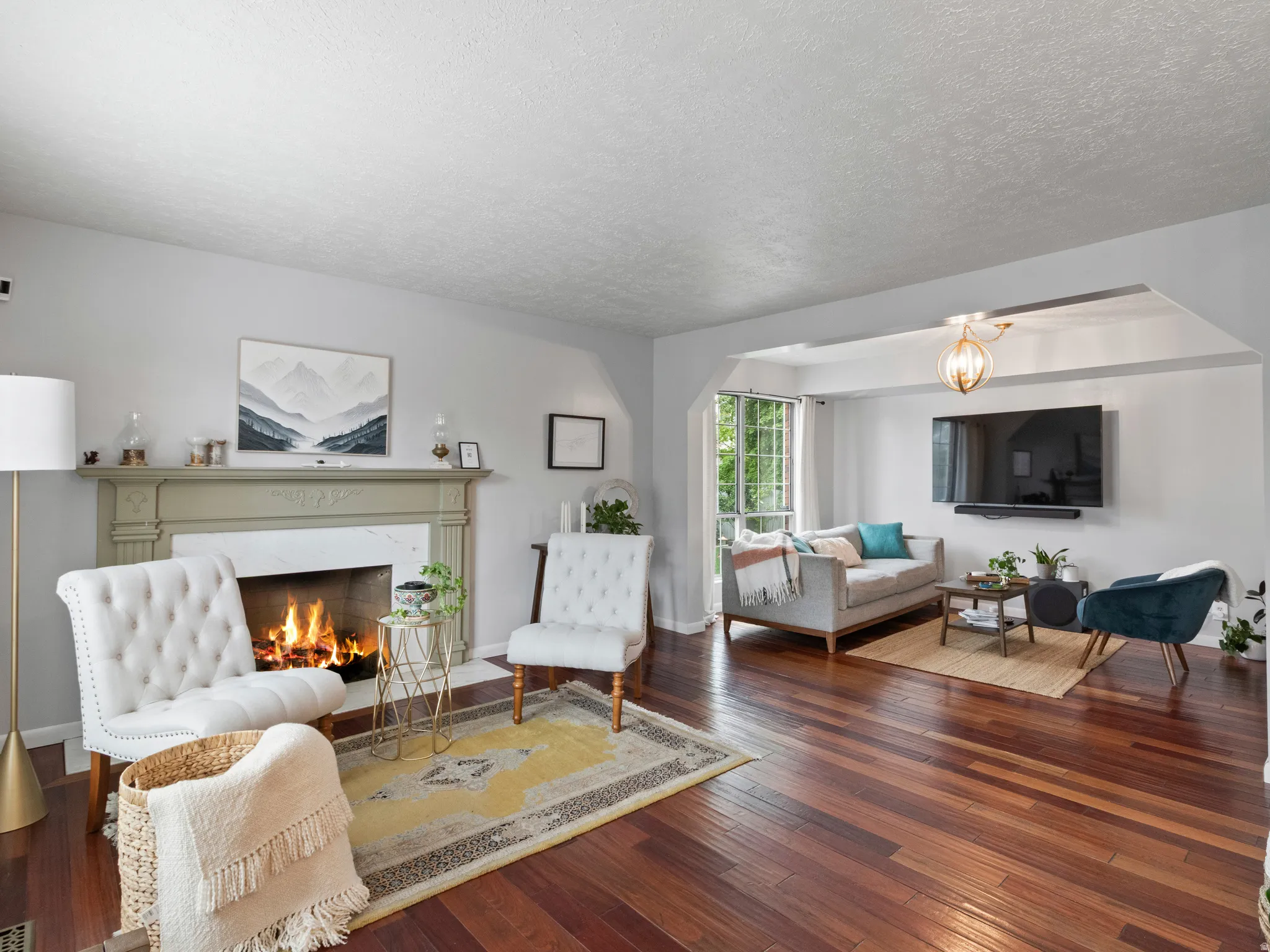 Living area featuring rich wood-finish flooring, a decorative fireplace with a light-toned mantel, light gray wall paint, and  entry to an additional sitting space