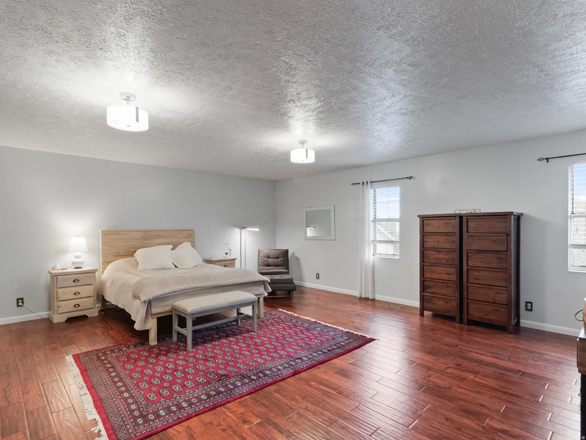 Spacious master bedroom featuring rich wood-finish flooring, light gray walls  and great lighting