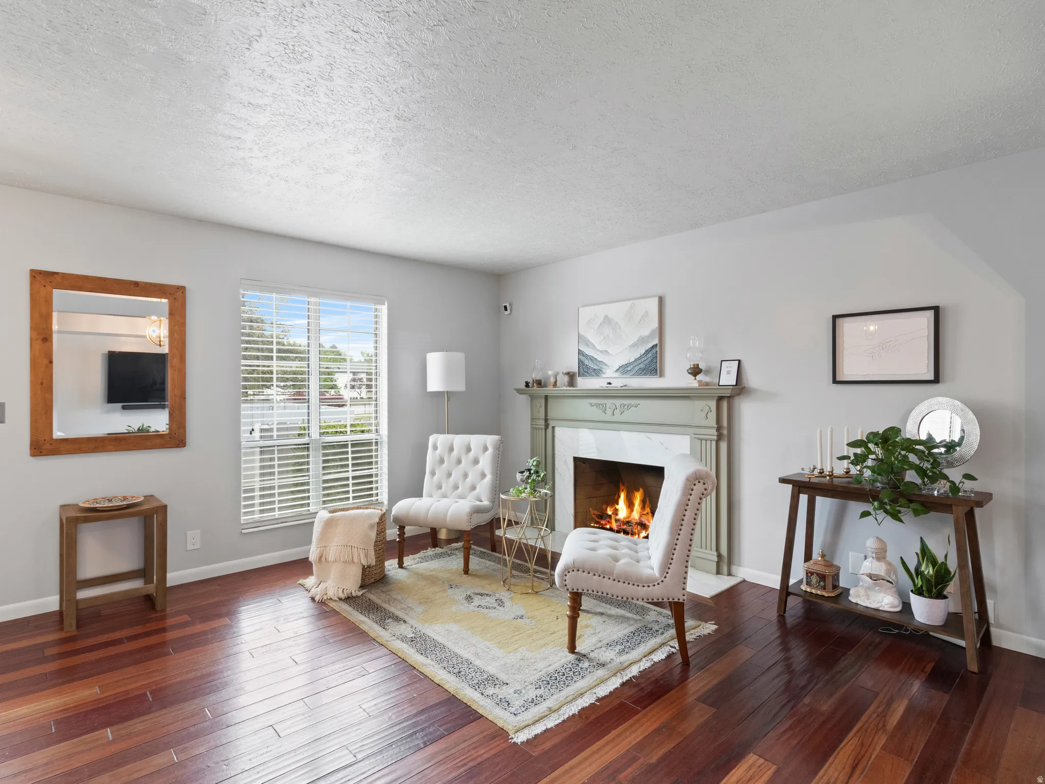 Living area featuring rich wood-finish flooring, a decorative fireplace with a light green mantel, and a large window