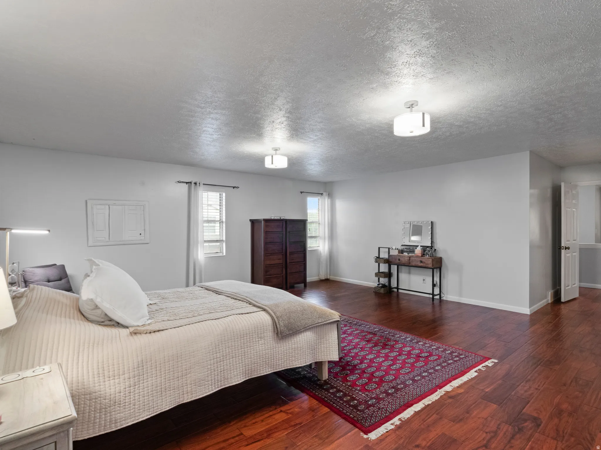 Spacious master bedroom featuring wood-finish flooring, light grey walls, and dual windows for natural illumination