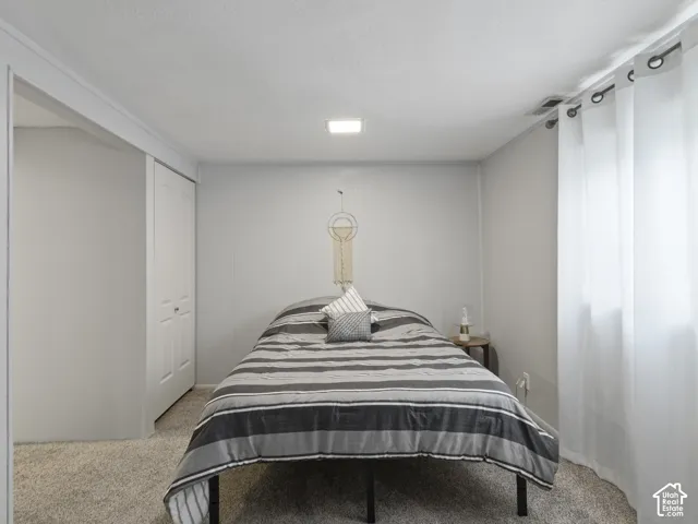 Studio bedroom with Carpeted floors. Featuring a white bi-fold closet door, textured ceiling, recessed lighting, and a large windows with white curtains