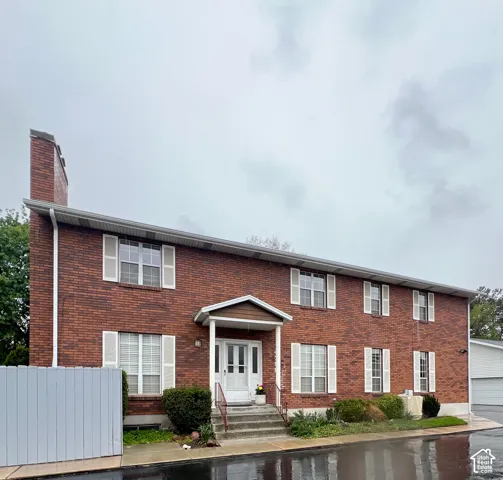 Brick exterior featuring a covered entry, white paneled door, and multiple windows with white shutters