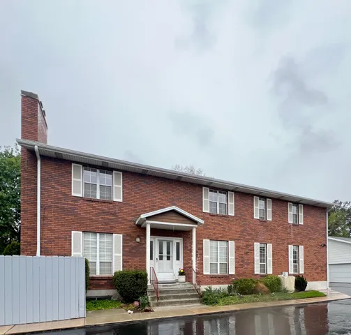 Brick exterior featuring a covered entry, white paneled door, and multiple windows with white shutters