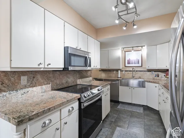 Kitchen featuring extensive white cabinetry, Granite countertops, stainless steel appliances, a stainless steel farmhouse sink, and tile flooring