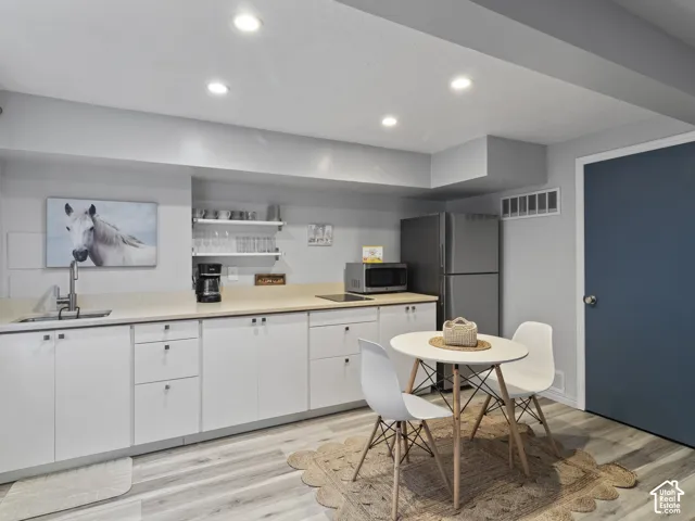 Contemporary kitchen area featuring extensive white cabinetry, light countertops, and laminate finish flooring