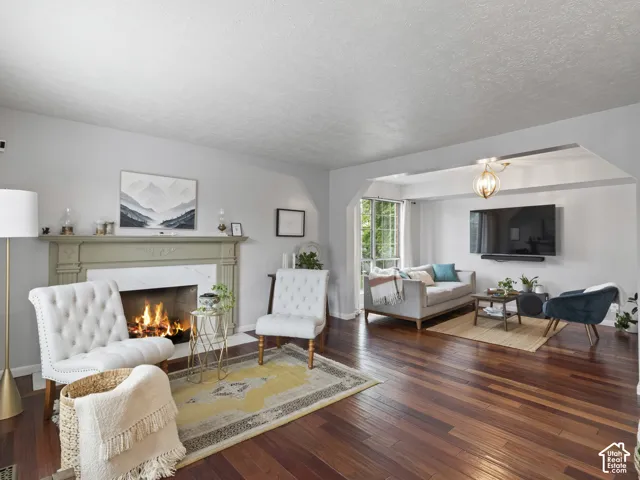 Living area featuring rich wood-finish flooring, a decorative fireplace with a light-toned mantel, light gray wall paint, and  entry to an additional sitting space