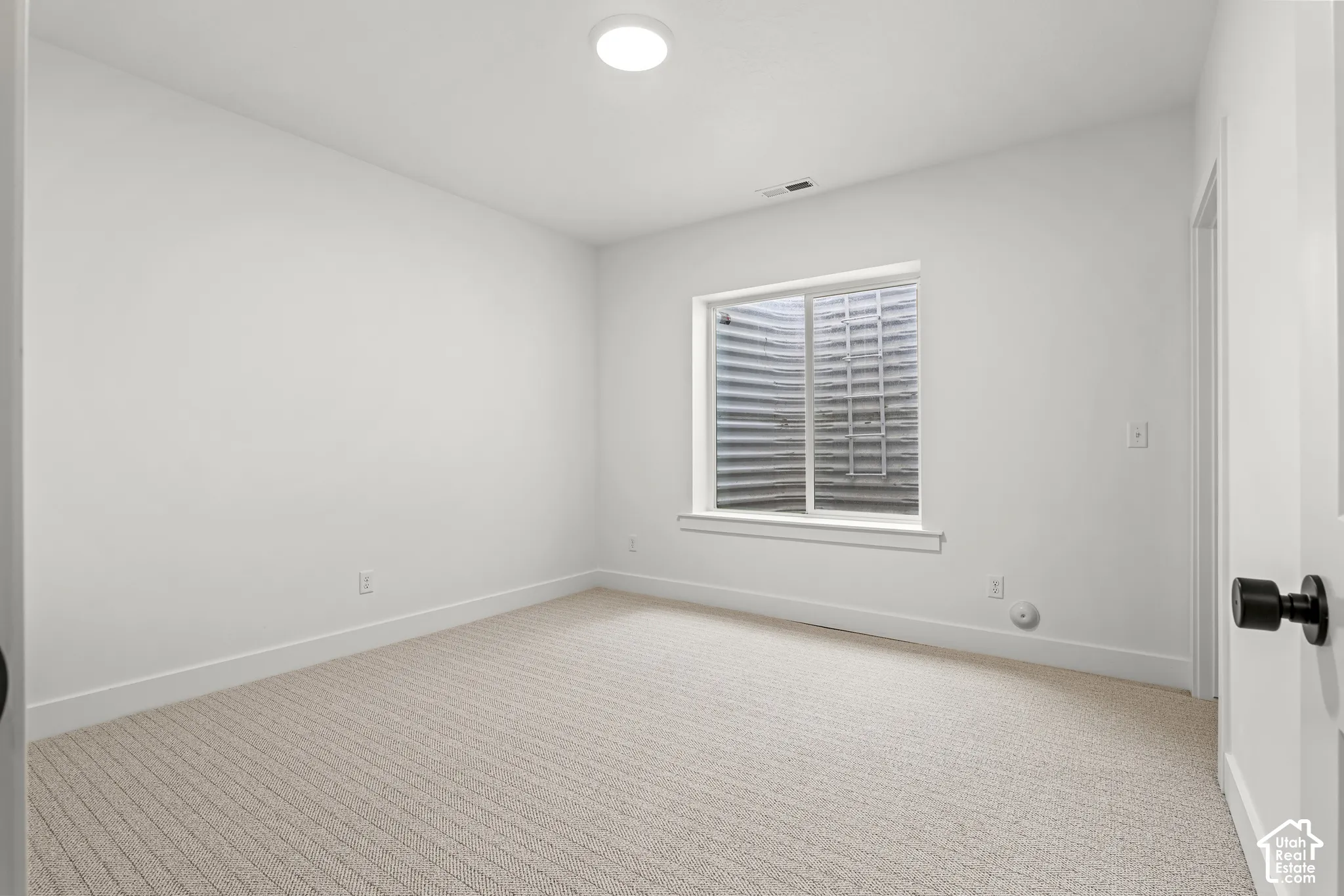 Carpeted room with a white window frame, clean white walls, and a recessed ceiling light fixture