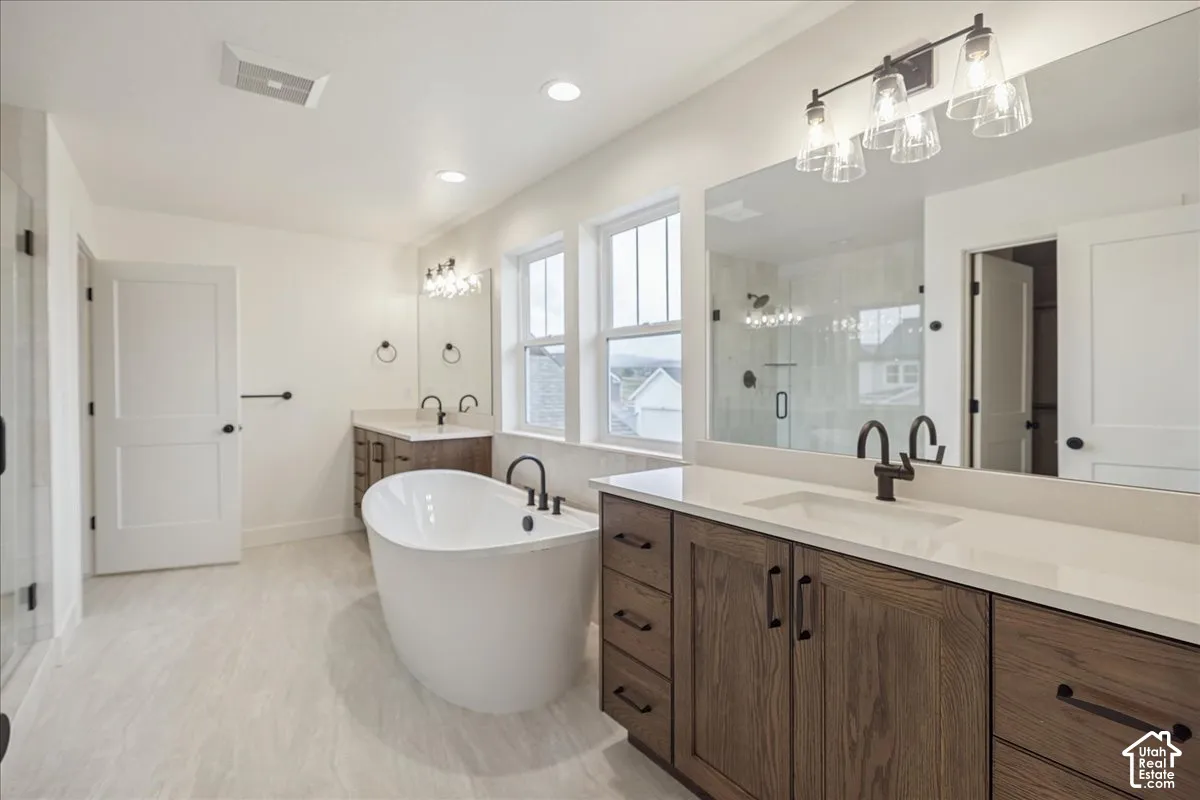 Primary Suite! Freestanding soaking tub with matte black faucet, dual-sink vanity with light-toned solid surface countertops, wood-finish cabinetry, full-width vanity mirrors, and recessed lighting