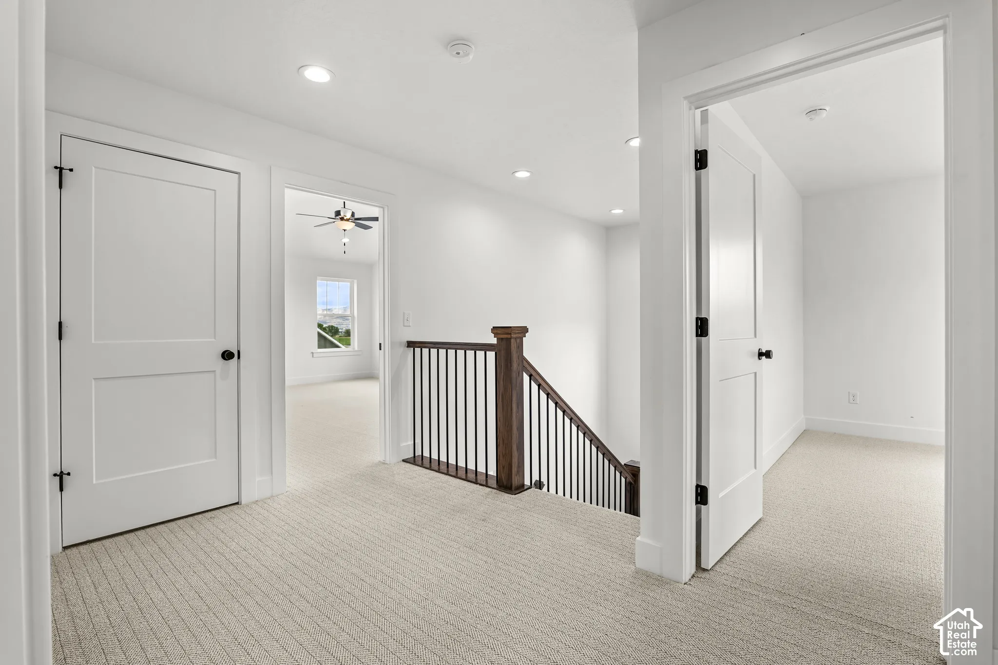 Upper-level hallway featuring light carpeting, recessed lighting, white paneled doors with black hardware, and a wood and black metal staircase railing