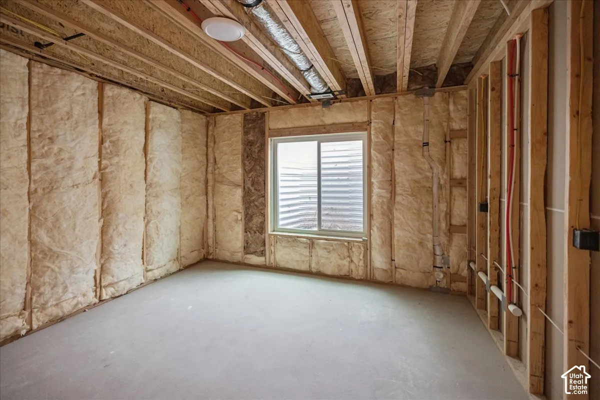 Unfinished space featuring exposed timber framing, insulation batts, concrete flooring, and a single sliding egress window with a corrugated metal window well