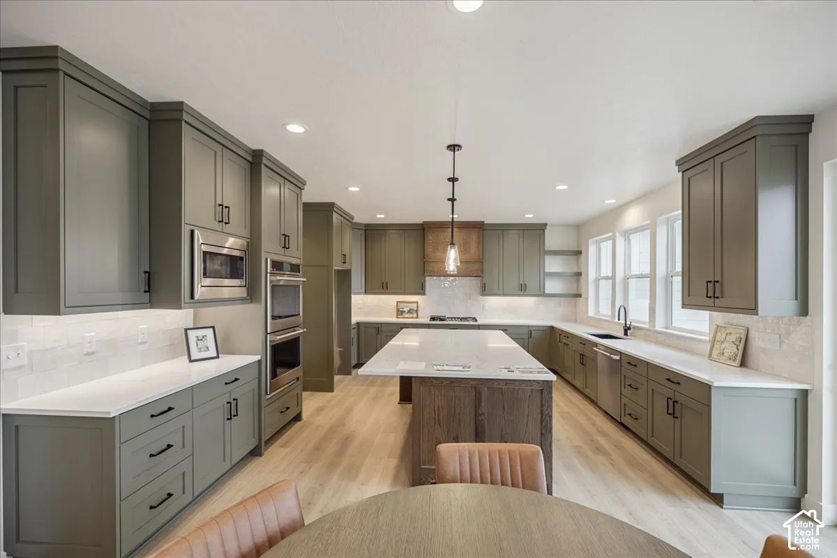 Kitchen featuring sage green cabinetry, a large central island with a wood-finish base, stone-style countertops, integrated stainless steel appliances, and wood-finish flooring
