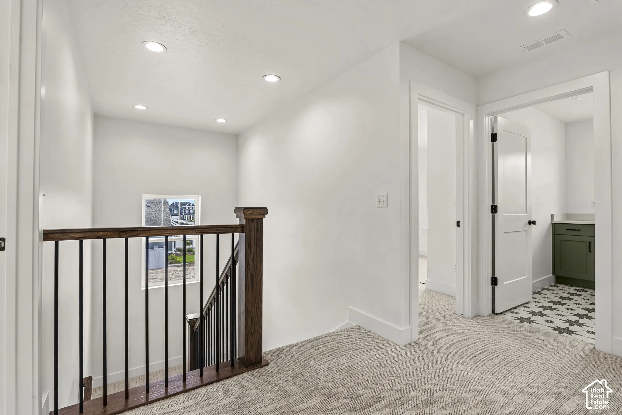 Upper-level hallway with neutral carpeting, recessed lighting, and a dark wood-finish railing with black balusters