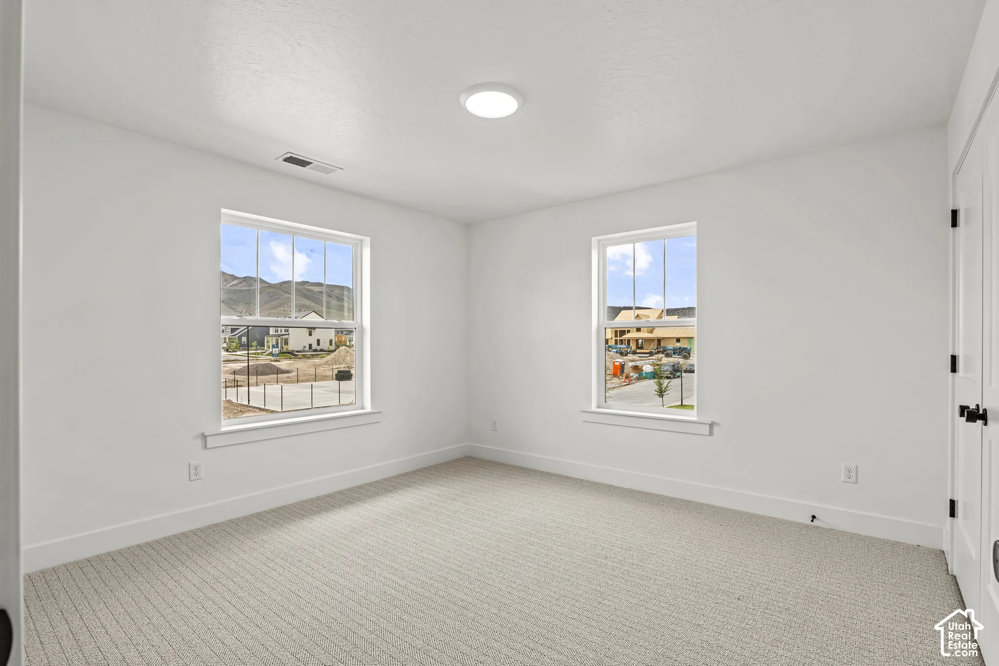 Bright room featuring two windows with mountain scenery, white walls, and neutral-toned carpeting