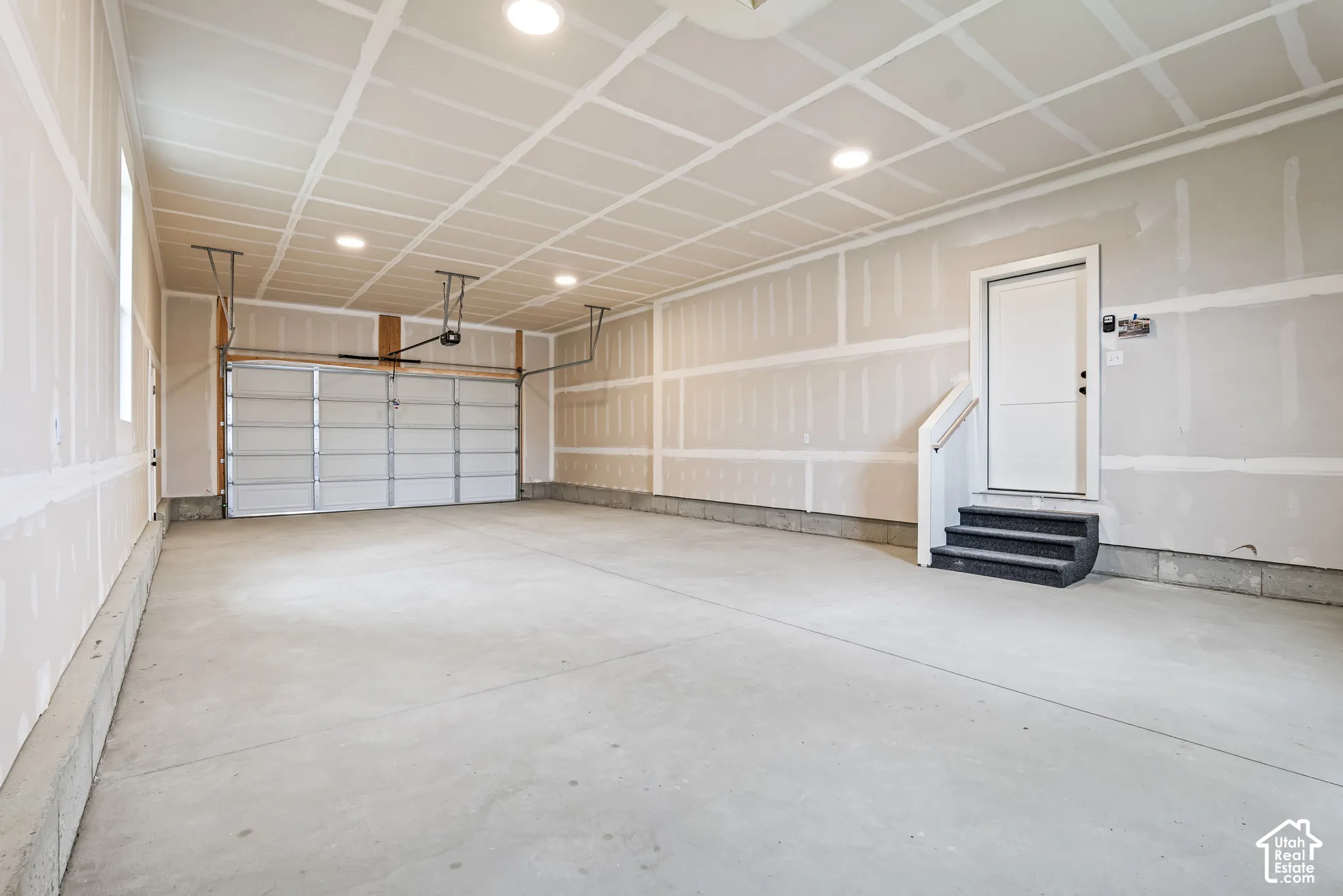 Spacious garage featuring a concrete floor, a large overhead garage door, recessed lighting, and a separate entry door with steps