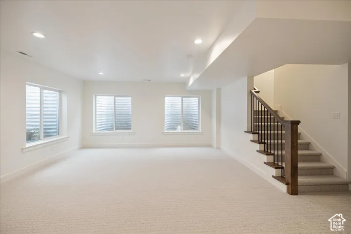 Neutral interior featuring recessed lighting, wall-to-wall carpeting, egress windows, and a staircase with stained wood handrails and metal balusters