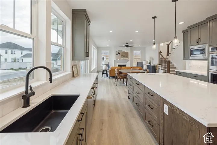 Kitchen featuring an oversized island with light-toned countertops, contrasting charcoal cabinetry, wood-finish flooring, recessed lighting, and a deep undermount sink with a matte black faucet