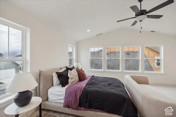 Primary Suite! Vaulted ceiling featuring a central multi-blade ceiling fan and multiple large windows with white trim