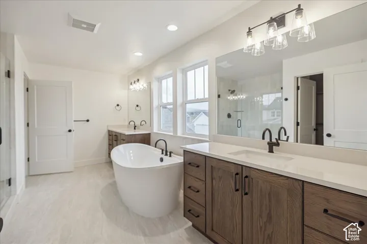 Primary Suite! Freestanding soaking tub with matte black faucet, dual-sink vanity with light-toned solid surface countertops, wood-finish cabinetry, full-width vanity mirrors, and recessed lighting
