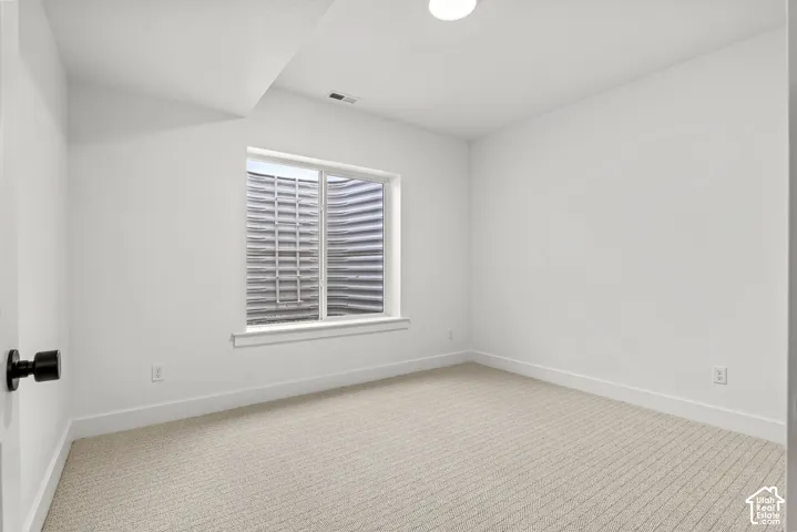Room featuring a textured carpet, white walls, and a window with a white frame and well guard