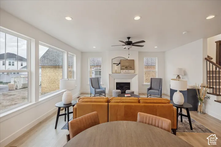 Open-concept living space featuring wood-finish flooring, recessed lighting, large picture windows, a central fireplace with a custom mantle, and a ceiling fan