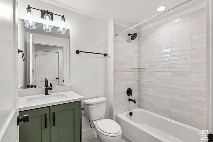 Bathroom featuring a vanity with a green cabinet and a white countertop, a toilet, and a tub with a shower