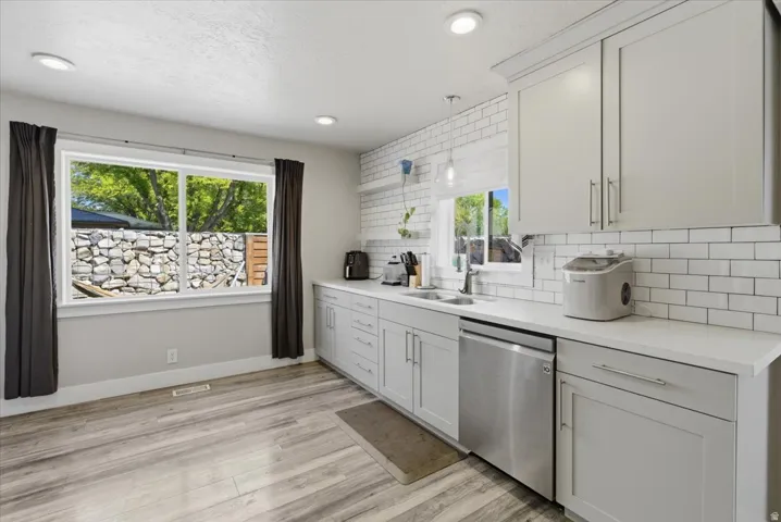 Contemporary kitchen featuring light gray cabinetry, a subway tile backsplash, stainless steel dishwasher, and wood-finish flooring