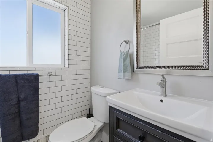 Bathroom featuring white subway tile walls, a window with natural light, a dark wood-finish vanity with an integrated sink, a contemporary single-handle faucet, and a decorative framed mirror