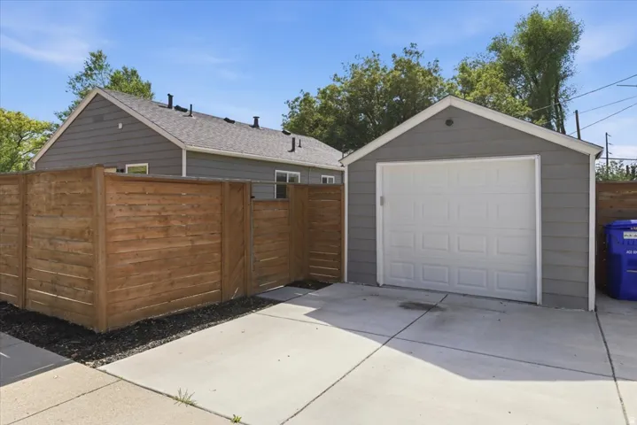 Detached garage with a white panel door, gray siding, and a gabled roof