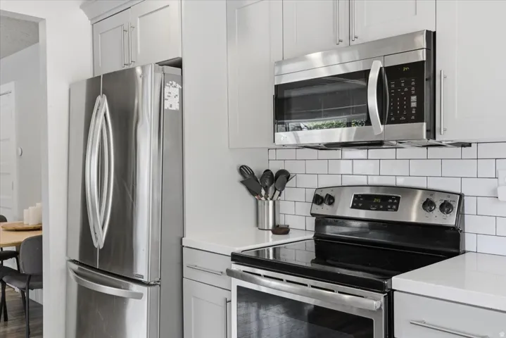 Contemporary kitchen featuring stainless steel appliances, white subway tile backsplash, light gray cabinetry, and white countertops