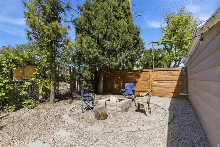 Gravel yard featuring a stone-lined circular fire pit area, a slatted wood fence, and mature trees