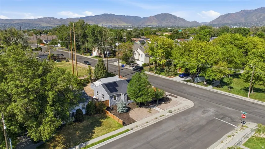 Corner lot residence featuring a light gray exterior, dark shingle roof with solar panels, and a brown privacy fence