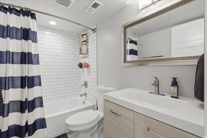 Bathroom featuring a subway tile shower surround, a white bathtub, and a light wood-finish vanity with an integrated sink
