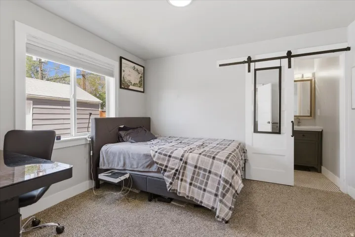 Bedroom featuring neutral carpeting, a large window with white trim, and a sliding barn door with a full-length mirror panel