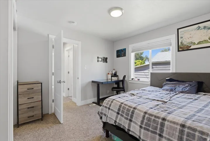 Bedroom featuring light gray walls, textured carpet flooring, and a window with white trim