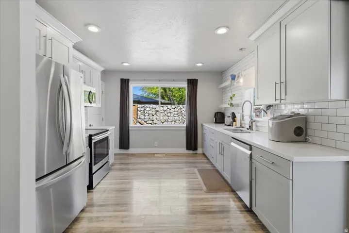 Modern kitchen featuring light gray cabinetry, stainless steel appliances, white countertops, a subway tile backsplash, and wood-finish flooring