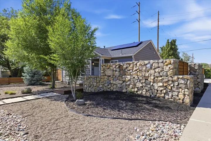 Exterior featuring a stone gabion wall, wood siding, and solar panels on the roof