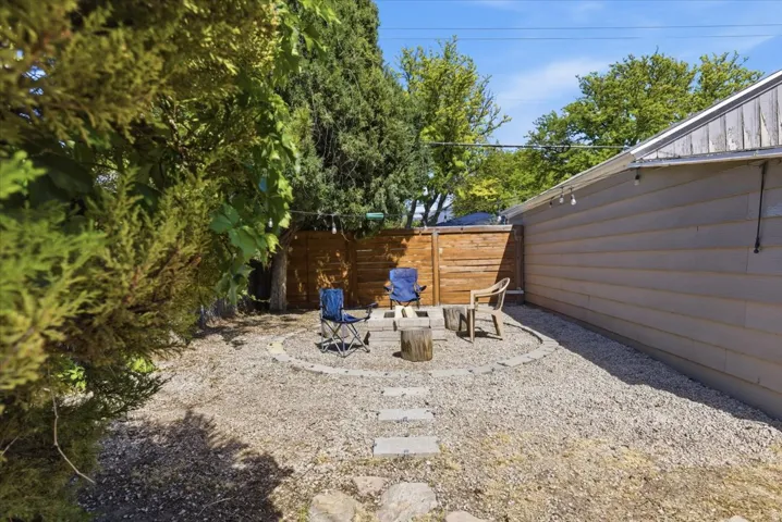 Landscaped backyard featuring a circular stone fire pit area with gravel ground cover