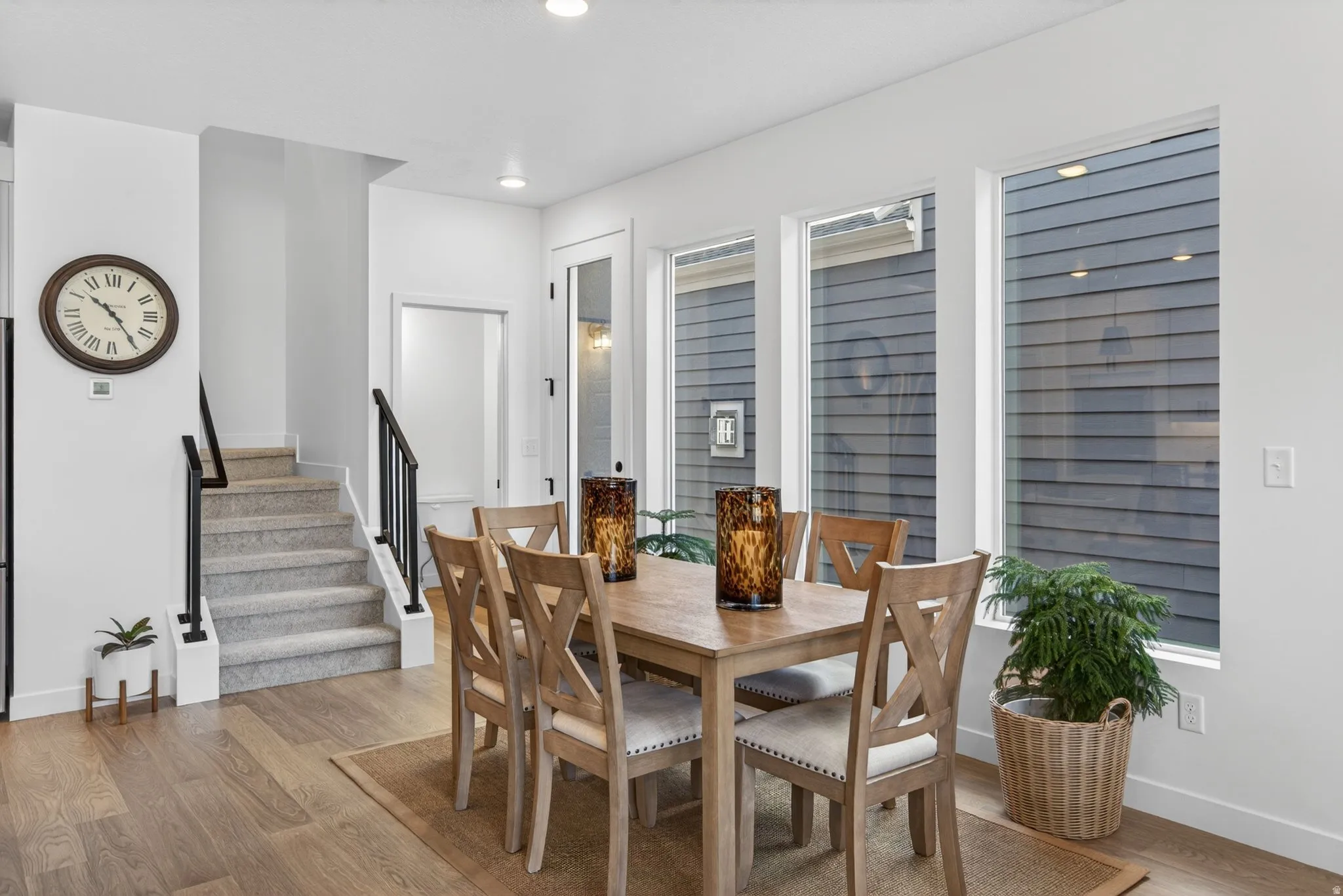 Dining area featuring wood-finish flooring, a wall of multiple windows, recessed lighting, and a staircase with black metal railings