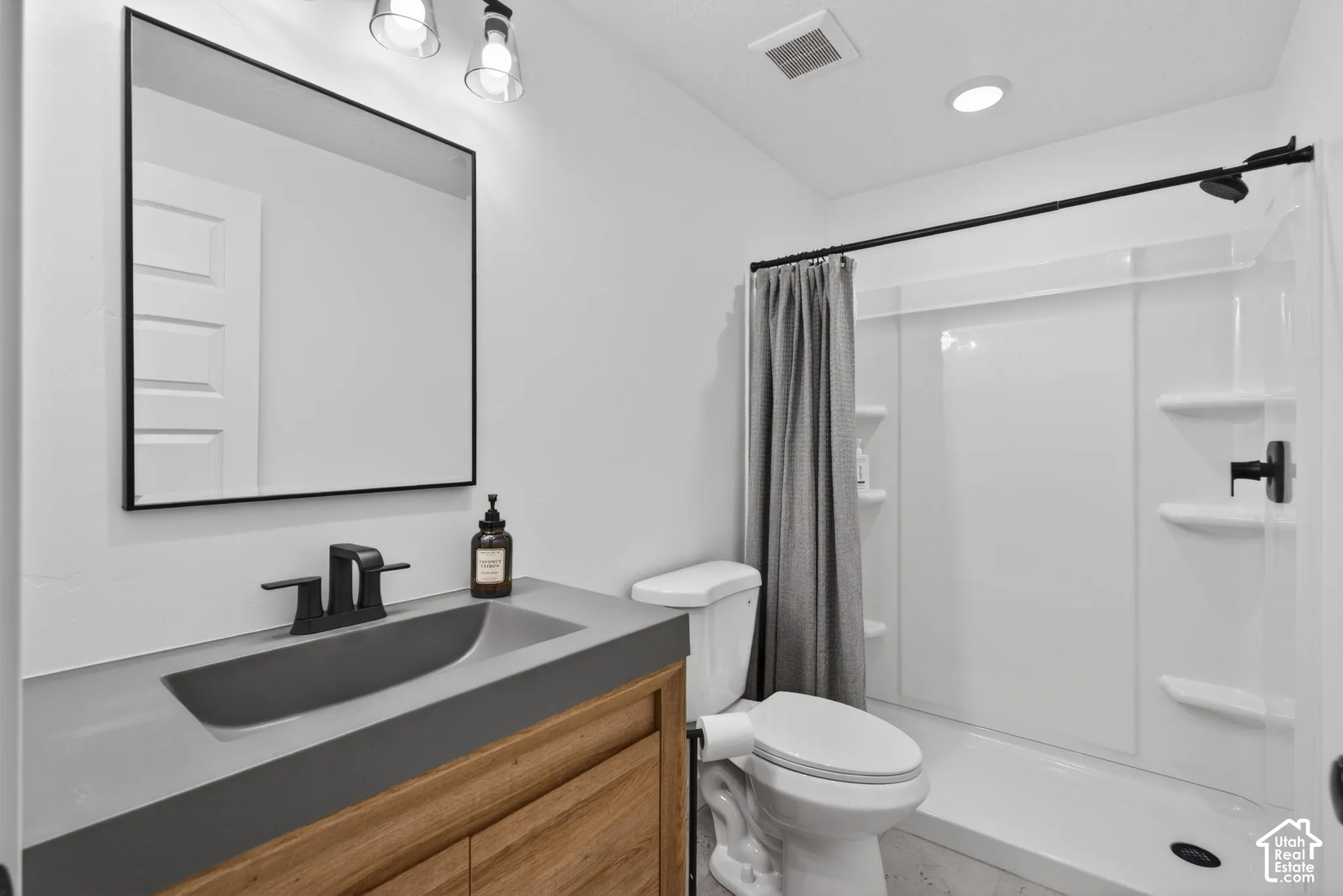 Bathroom featuring a wood-finish vanity with integrated sink, black fixtures, and a framed mirror
