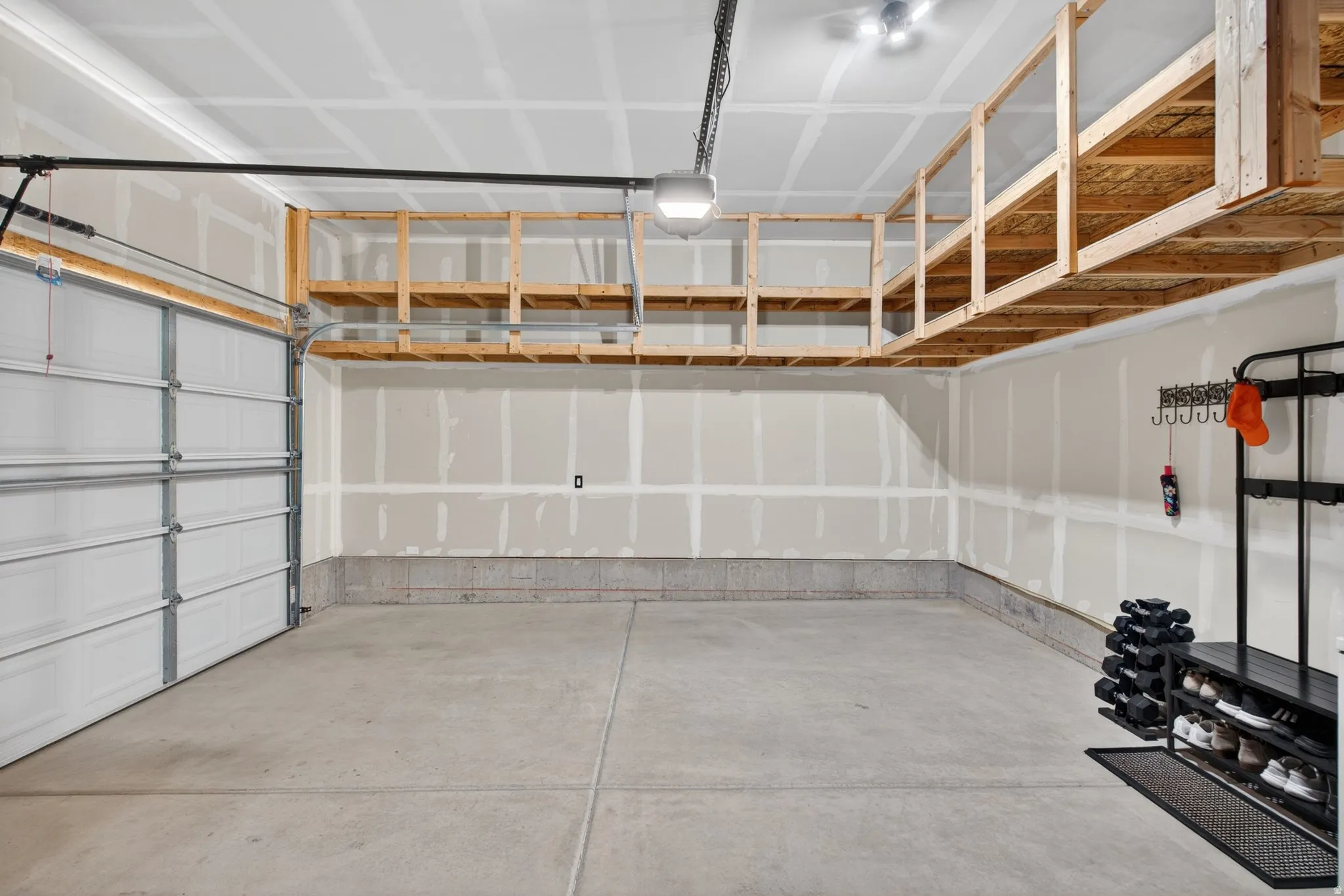 Spacious garage featuring a concrete floor, overhead wood-frame storage shelving, and a white paneled garage door