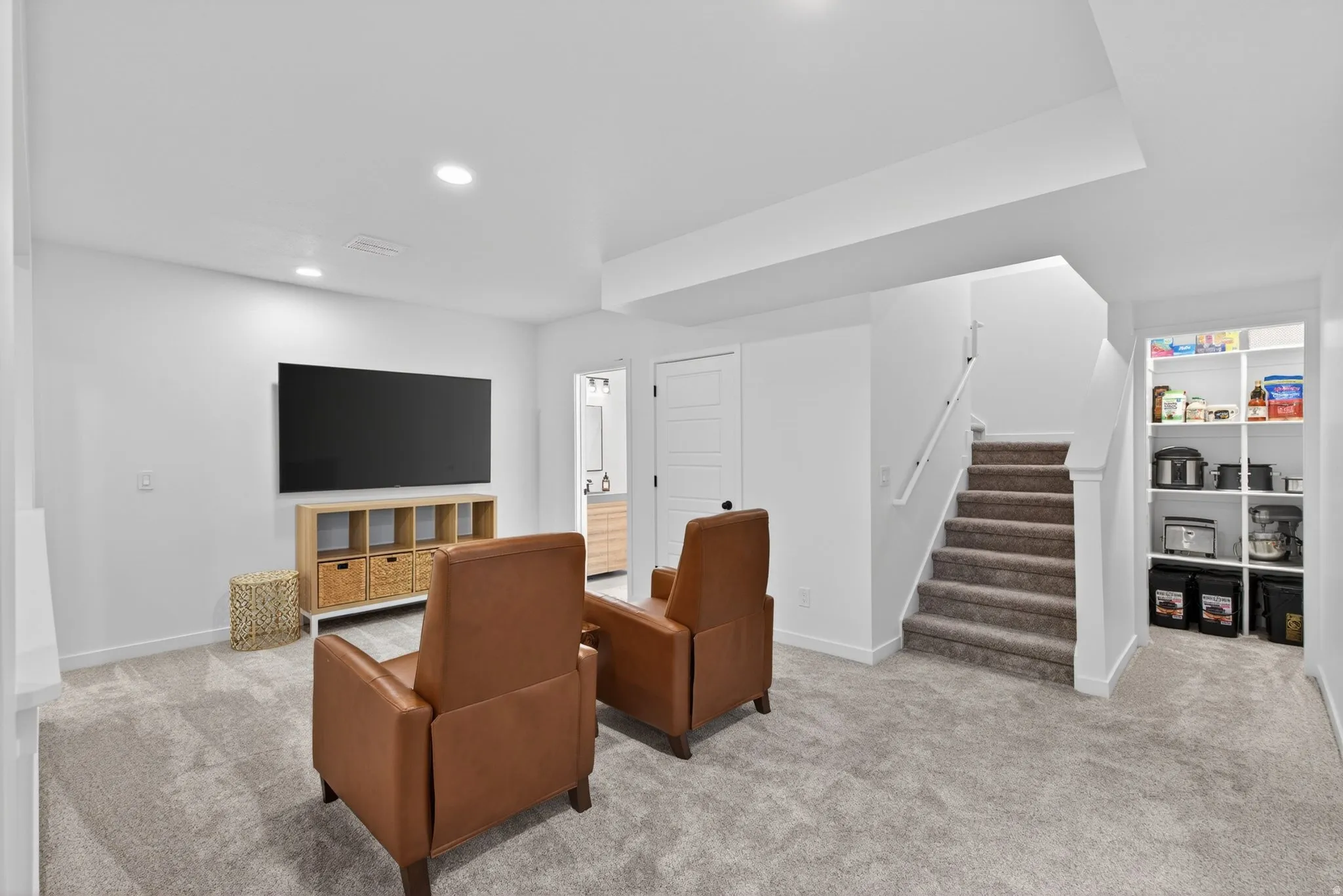 Carpeted recreation room featuring recessed lighting, a built-in shelving unit, and a carpeted staircase with a white handrail